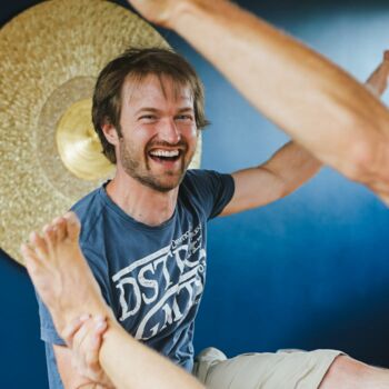 Junger Mann in der Yogaausbildungsklasse übt mit dem Partner eine Gleichgewichtsübung